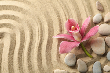 Fototapeta na wymiar Orchid and stones on sand background, top view. Zen concept