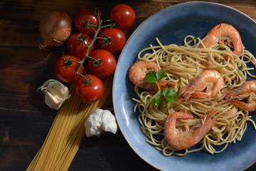 Shrimp with spaghetti on a blue clay plate next to a bunch of tomatoes