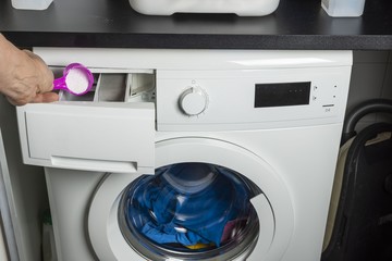 Close up view of male hand lay detergent into washing machine.