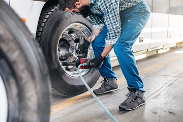 Mechanic worker changing tires on bus. Vehicle repair service.