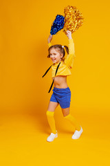 cute cheerleader girl in a yellow tank top and blue shorts is dancing with pompons in her hands