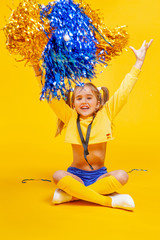 cute cheerleader girl in a yellow tank and blue shorts throws up pompons
