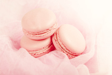 Delicious french dessert. Three gentle pastel soft pink cakes macaron or macaroon on a gentle airy fabric