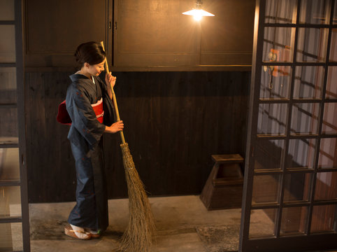 Mid Adult Japanese woman in kimono sweeping with broom at entrance