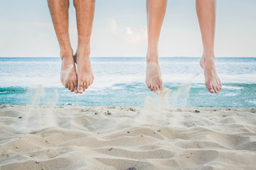 Bare feet of a man and a woman jump in the air on a sandy beach against the background of the sea
