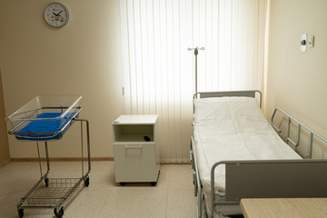 an empty postpartum ward with a bed for a woman in labor and a newborn. The end view, opposite the window. Daylight.