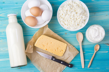 Fresh milk, cottage cheese, sour cream and cheese on paper, as well as eggs in a bowl lie on a blue wooden table. Natural, healthy, calcium-rich food