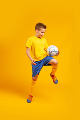 boy plays soccer ball in studio on a yellow background