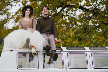 Romantic and happy caucasian couple in casual wedding clothes hugging near the vintage bus at the city streets. Love, relationships, happiness, urban concept. Man and woman celebrate their marriage.