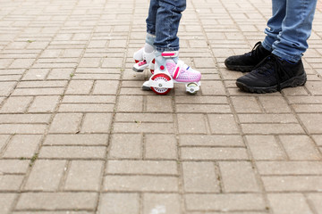 Dad teaches his little daughter to ride four-wheeled roller skates. The father supports the child by the hands, feet of the father and the child in skates. Focus on the rollers. Father's day, family 