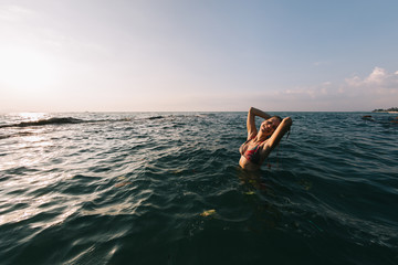 Girl with long hair swims in the sea, splashes water on a background of a sunset sky