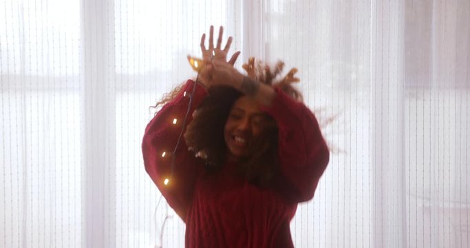 Black woman wearing reindeer antlers headband dancing with Christmas lights