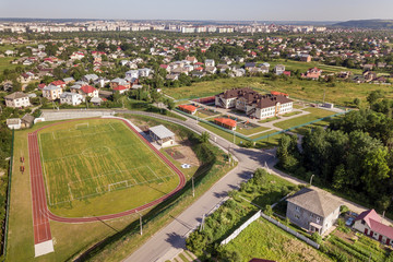 Fototapeta na wymiar Aerial view of a football field on a stadium covered with green grass in rural town area.