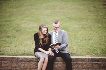 View of a couple wearing formal clothes while reading a book together in a garden