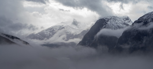 Wysokie szczyty górskie pokryte gęstą mgłą - obrazy, fototapety, plakaty