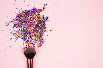 Closeup of professional cosmetic makeup brush with explosion of shiny colorful sparkles on bright pink background with copyspace for your text. Creative make-up concept