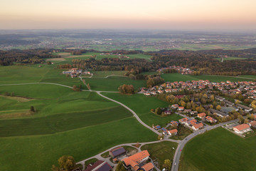 Aerial view of small town with red tiled roofs among green farm fields and distant forest in summer.
