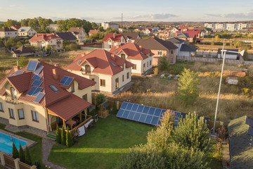 Aerial view of a residential private house with solar panels on roof and wind generator turbine.