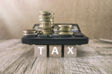 Wooden blocks with the word TAX.  calculator and money. Tax planning, tax refund or Tax concept.