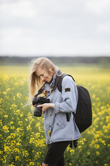Naklejka na ściany i meble Side view of smiling mature woman in casual clothing viewing photos on digital camera while standing among field with yellow flowers. Concept of photography and working process