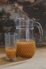 Pitcher with  glass and orange juice on photographed with natural light on brown textured background.