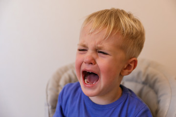 Portrait of a crying little boy with blond hair. The boy is sad. His mouth is wide open.
