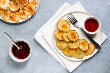 Trendy pancake cereal meal. Tiny baked pancakes with berry jam on white plate.. Breakfast food at home. Table top view, flat lay