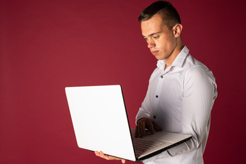 Confident business expert. Confident young handsome man in shirt holding laptop and smiling while standing on a red background