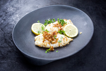 Fried calamari tubes in breadcrumbs breading with lemon slices and herbs offered as closeup on a modern design plate