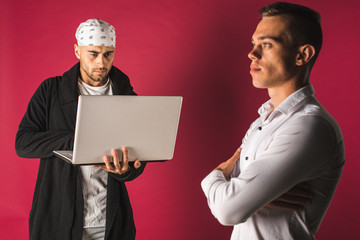 portrait of two young people, one working on computer the other in medical protective mask isolated on red background. sociability, pandemic, protection