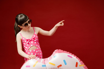 Isolated shot of charming little girl in sunglasses posing in studio with rubber ring going to have swim in sea during vacations. Pretty female child holding swimming inflatable circle