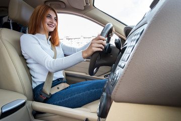 Young redhead woman driver driving a car smiling happily.