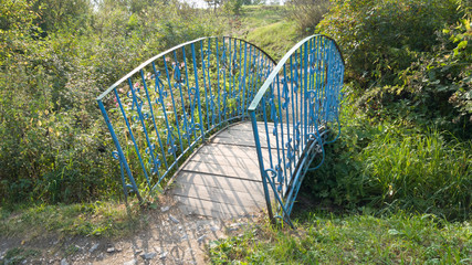 Old small blue bridge over the river. A trip to the countryside. Bent metal