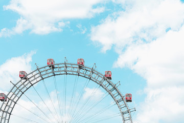 Gray ferris wheel with red booths against a blue sky.