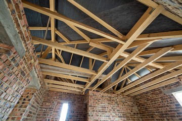 Obraz premium Attic space of a building under construction with wooden beams of a roof structure and brick walls. Real estate development concept.