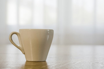 cup of coffee and book on a wooden table, window in the background
