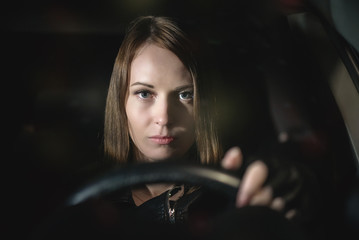 Young woman is holding her hands on the steering wheel and driving a car.
