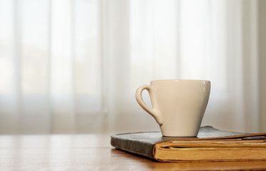 cup of coffee and book on a wooden table, window in the background