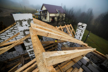 Fototapeta premium Top view of roof frame from wooden lumber beams and planks on walls made of hollow foam insulation blocks. Building, roofing, construction and renovation concept.