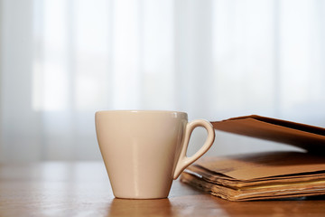 Fototapeta premium cup of coffee and book on a wooden table, window in the background