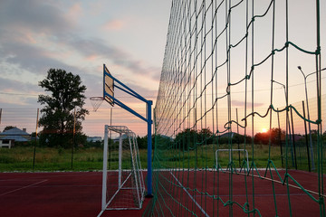 Outdoors mini football and basketball court with ball gate and basket surrounded with high protective fence.