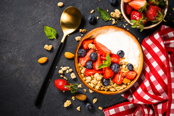 Greek yogurt granola with fresh berries on black stone table.
