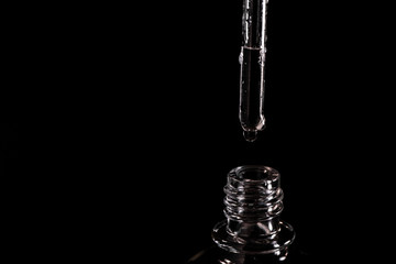 Close-up on a pipette with fluid and neck of a vial on black background