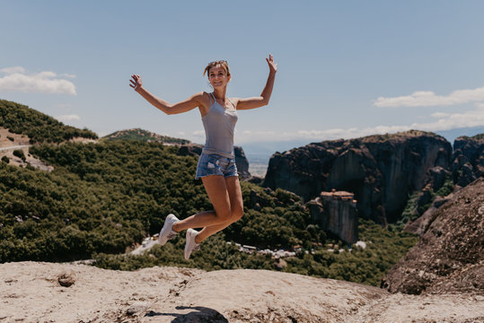 Portrait of the beautiful young woman in jump with hands wide open in Greece on Meteora mountains background. A girl jumping in front of Meteora&acute;s mountainous landscapen, Monasteries of Meteora
