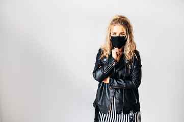 Protect yourself during an epidemic. Young blond woman in a leather jacket in a medical mask on her face on a white background