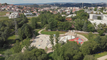 Fototapeta na wymiar Amazing aerial view of the skate park in Santo Tirso city in Portugal with many skaters and bmx bikers on it. The Geao Urban Park with high school building in background.