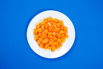 Tasty sweet sliced papaya fruit in a white bowl isolated on blue background