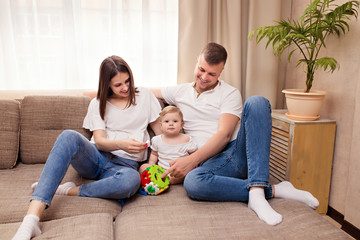 Happy family, mom and dad play with little daughter, spending time together and having fun on the couch