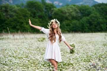 Beautiful young girl with curly hair in chamomile field.  Beautiful girl with chamomile wreath on...