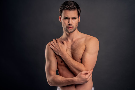 Handsome young bearded man isolated. Cropped image of shirtless muscular man is standing on gray background. Man holding his elbow. Experiencing elbow pain.